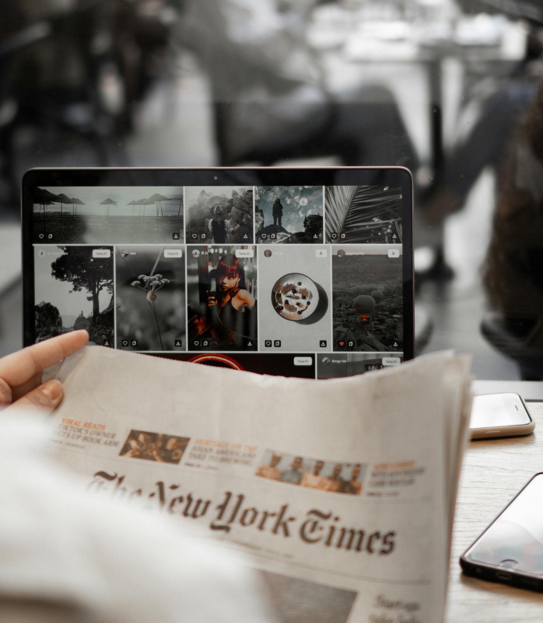 A person reading a newspaper while browsing images on a laptop, symbolizing remote work lifestyle.