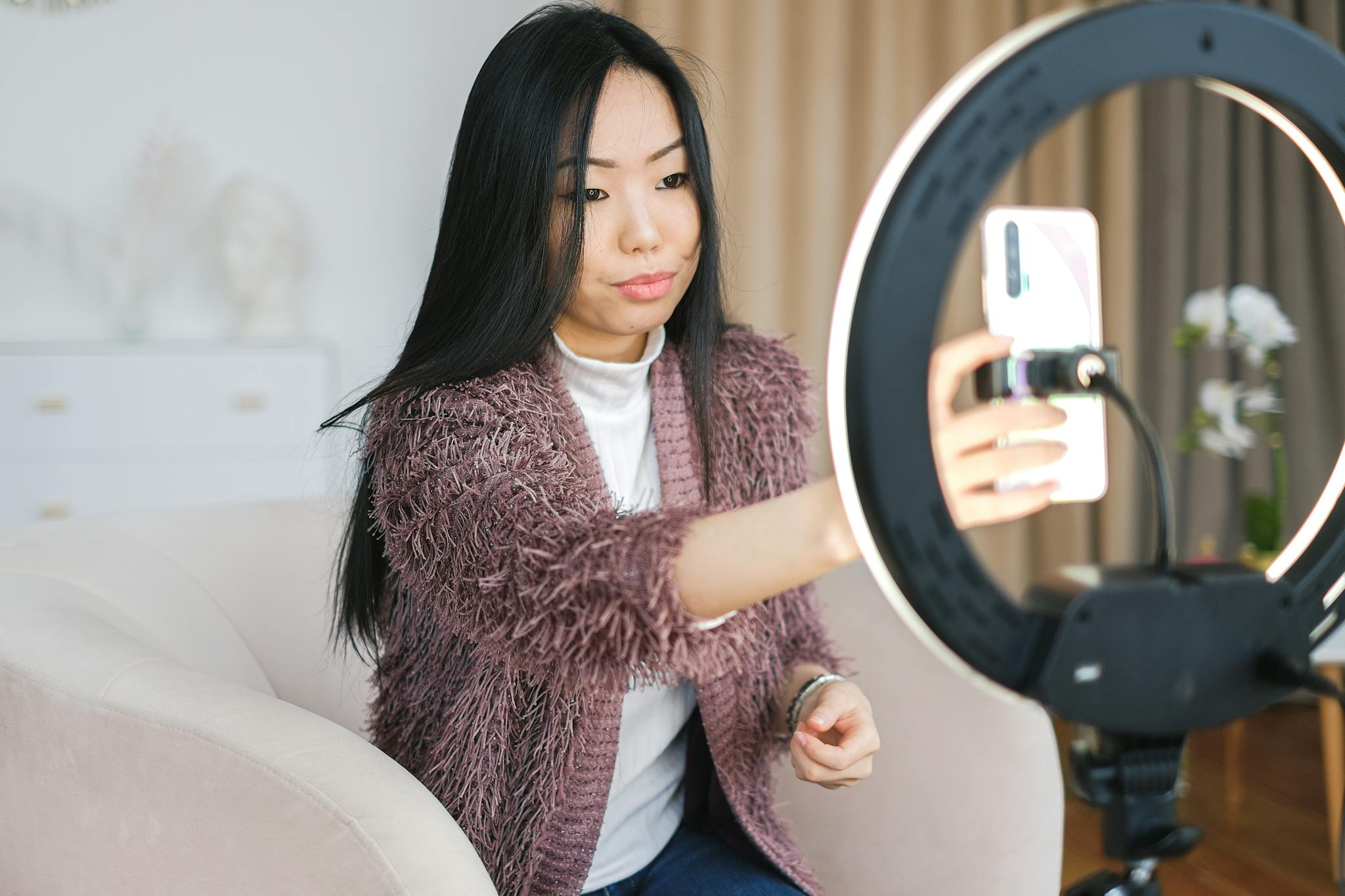 Asian woman using smartphone and ring light for vlogging indoors.