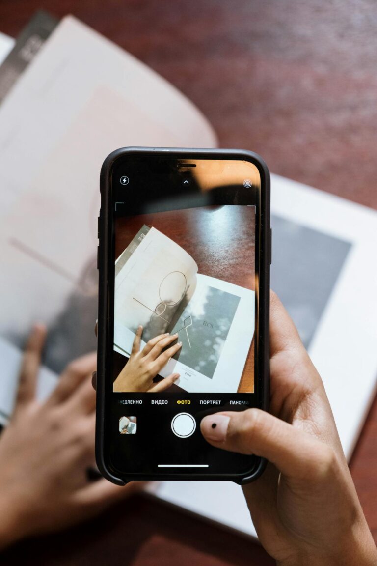 Close-up of hands photographing a magazine page using a smartphone, focusing on creativity and technology.