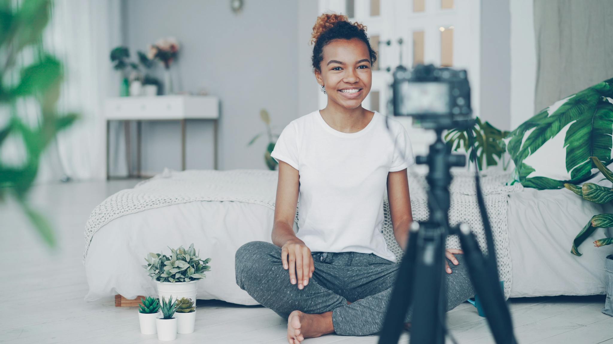 Smiling young woman vlogging from home, surrounded by houseplants and decor.